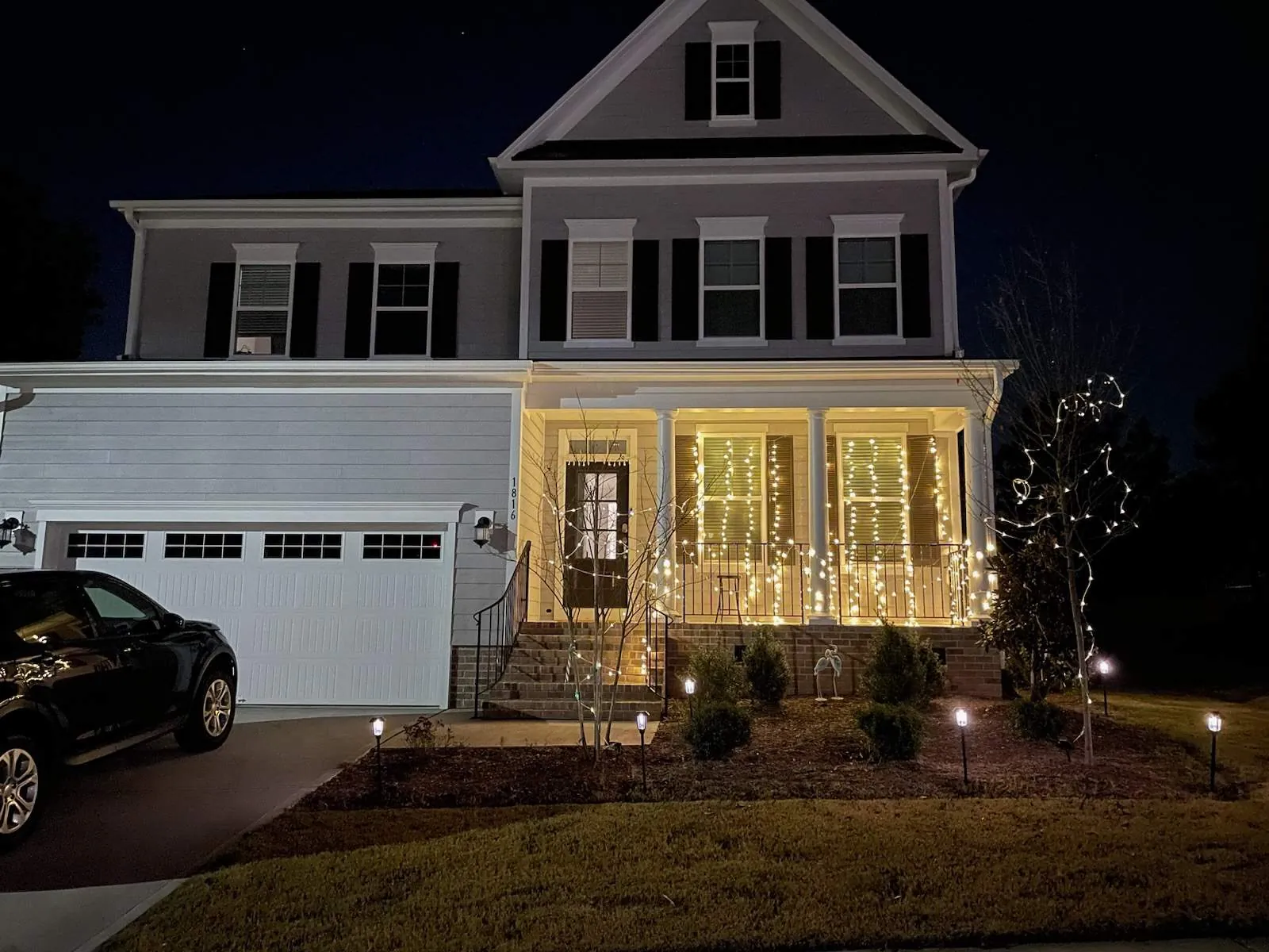 Two-story home in Cary at night with warm white Christmas lights on the front porch and a lit tree
