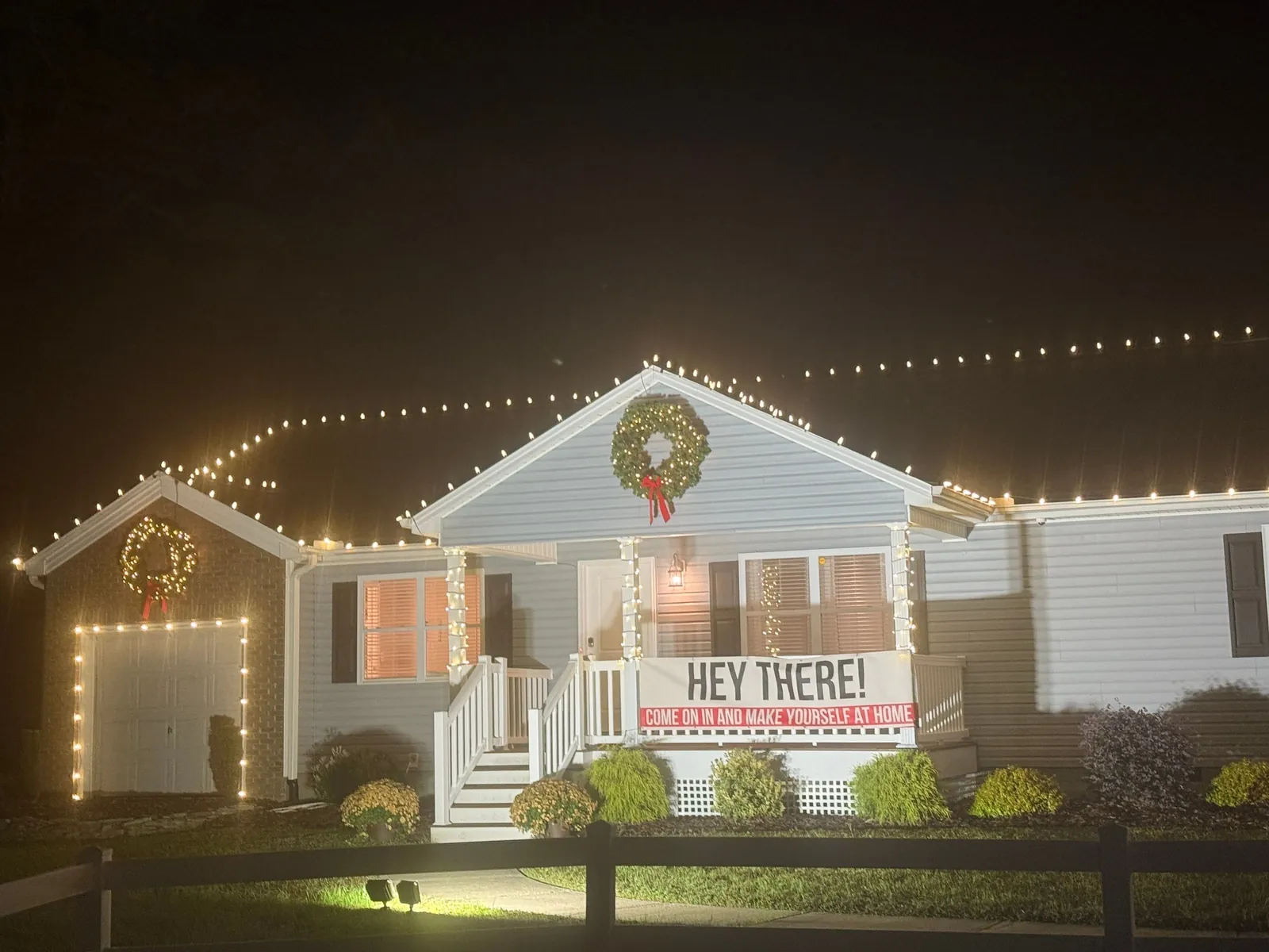 Ranch home at night with warm white roofline Christmas lights, wreaths and lit garage outline