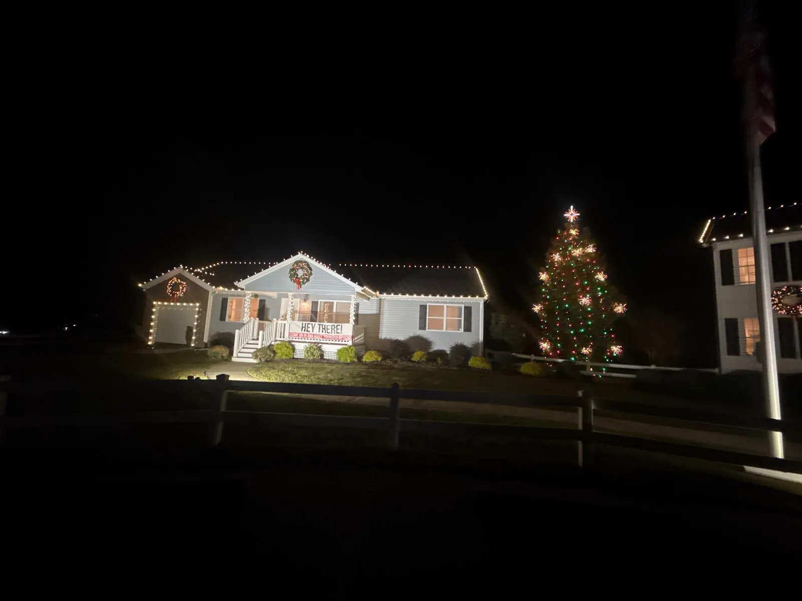 Home with white roofline Christmas lights and a lit evergreen tree at night