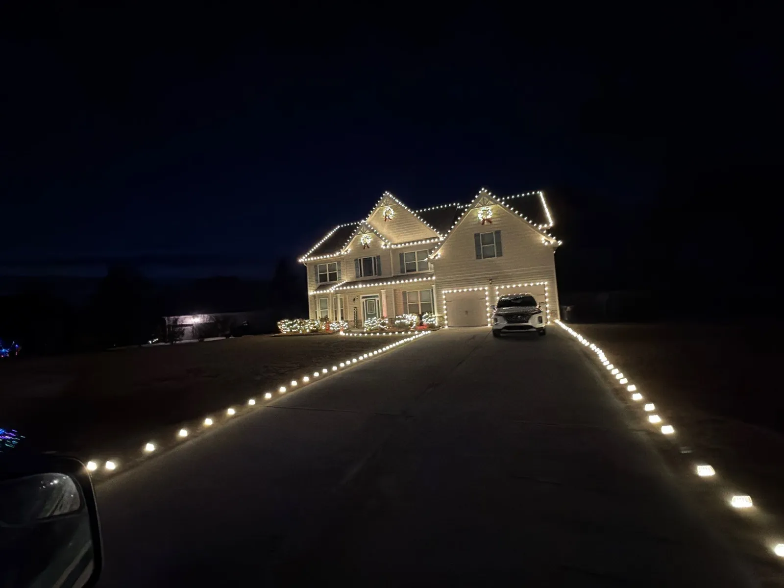 Long driveway lined with white Christmas lights leading to a lit two-story home