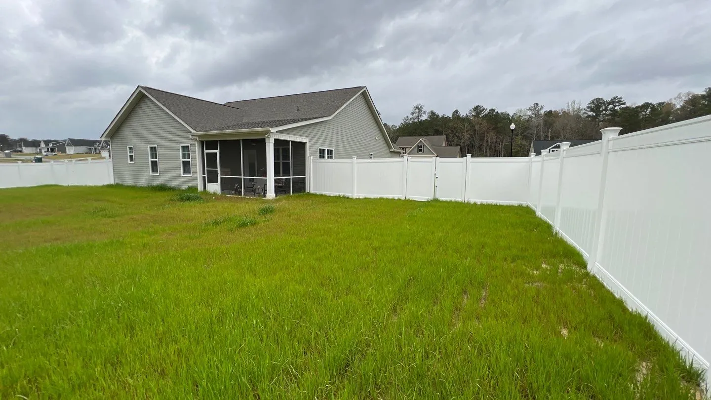Green lawn inside a white vinyl privacy fence behind a home