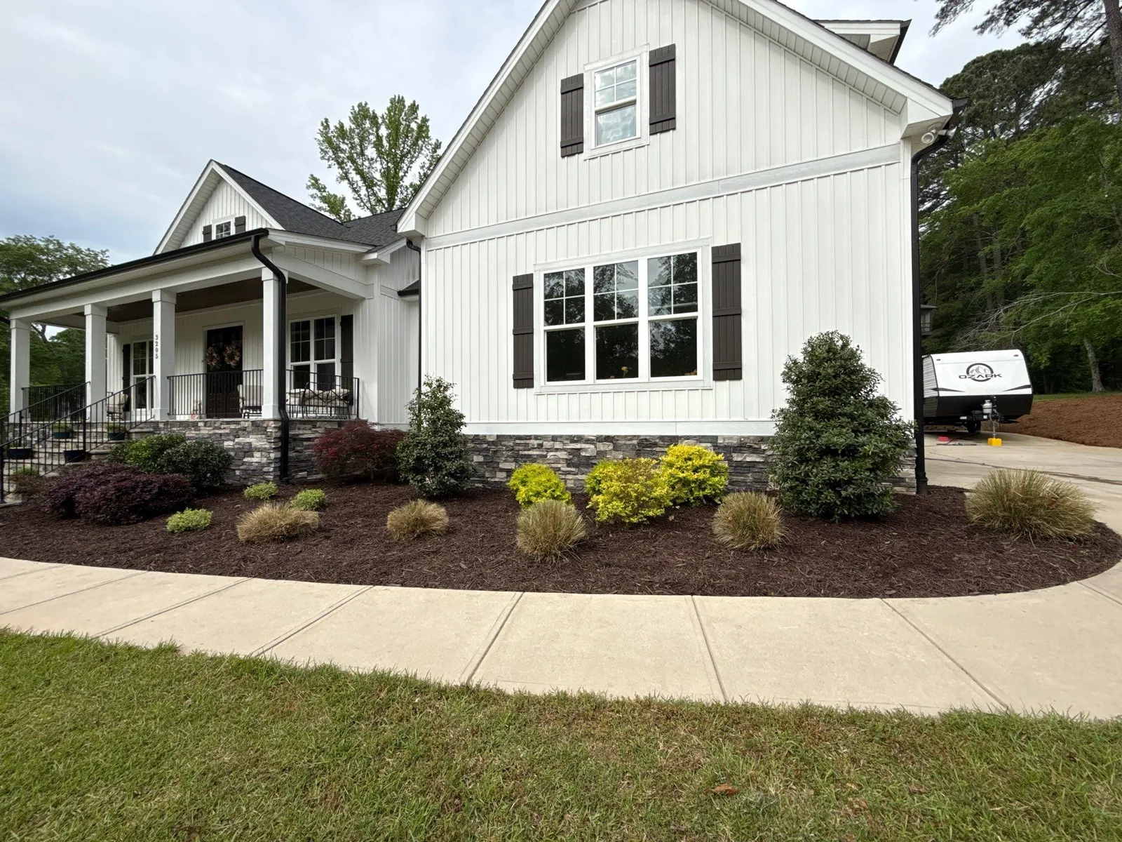 New foundation planting with shrubs, ornamental grasses and dark mulch in front of a white farmhouse-style home in Sanford, NC