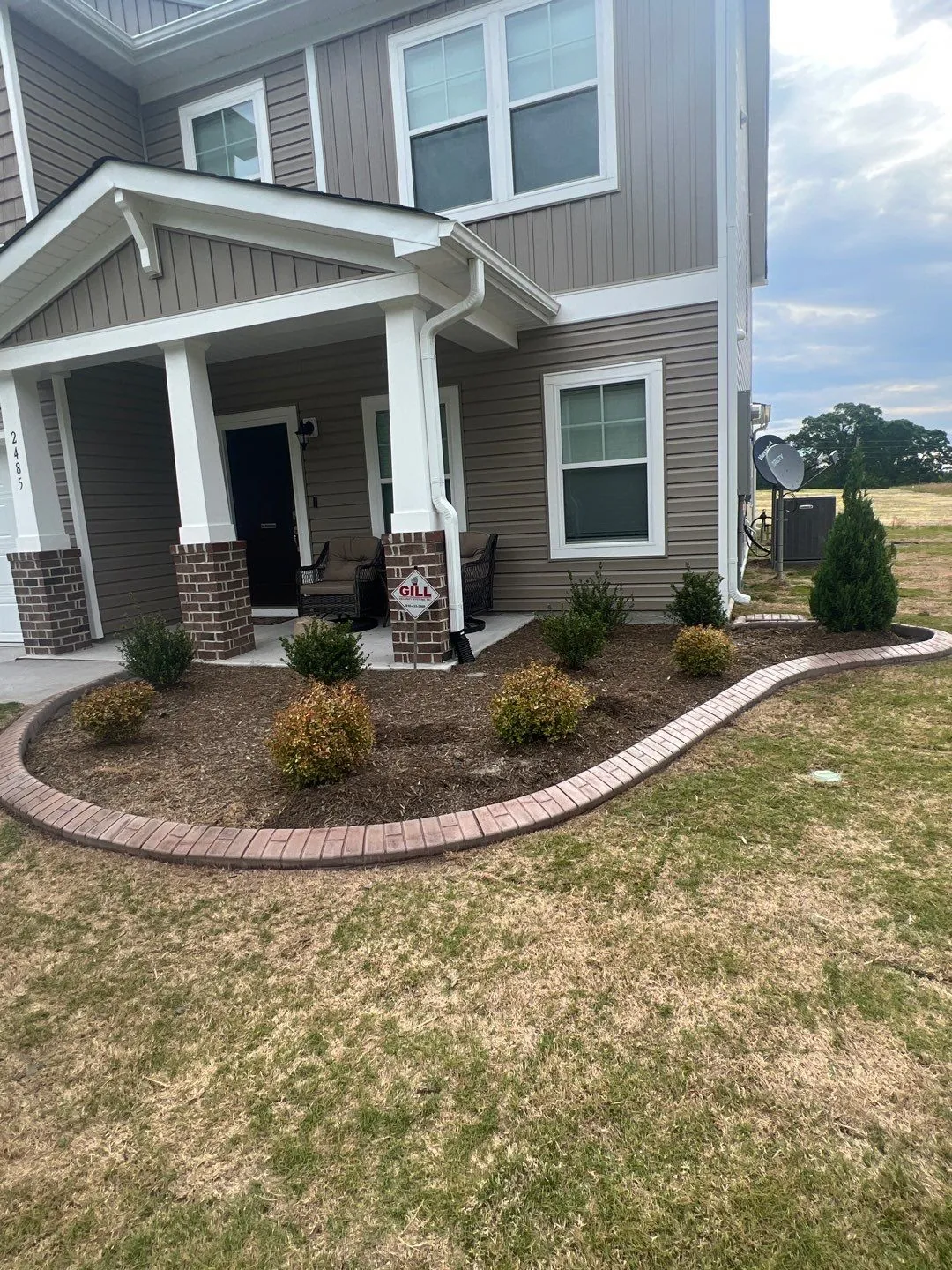 Front bed with new shrubs and brown mulch inside a curved brick edging border